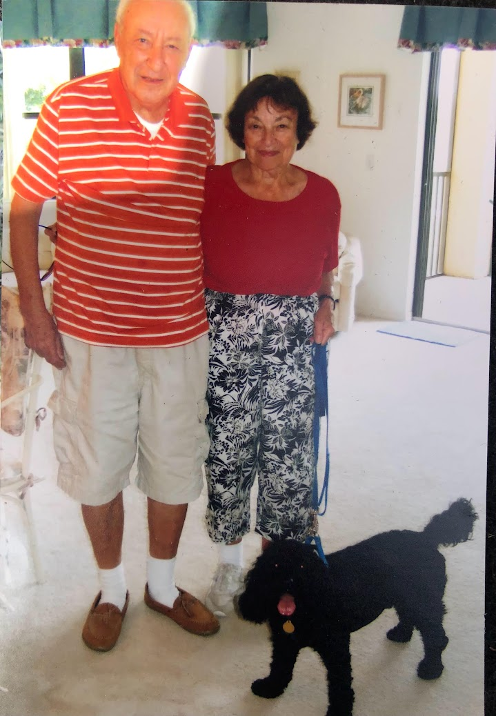 Grandparents wearing red, standing together with a black dog